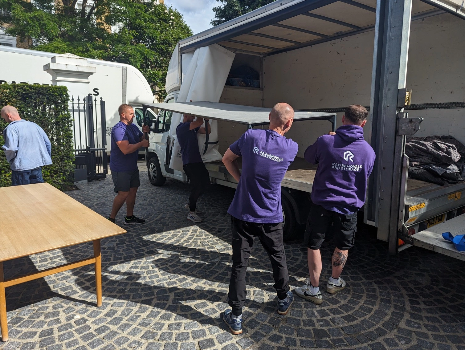 The RAD Removals and Storage team carefully loading a large dining table onto their van, ensuring secure transport for a home renovation project in London